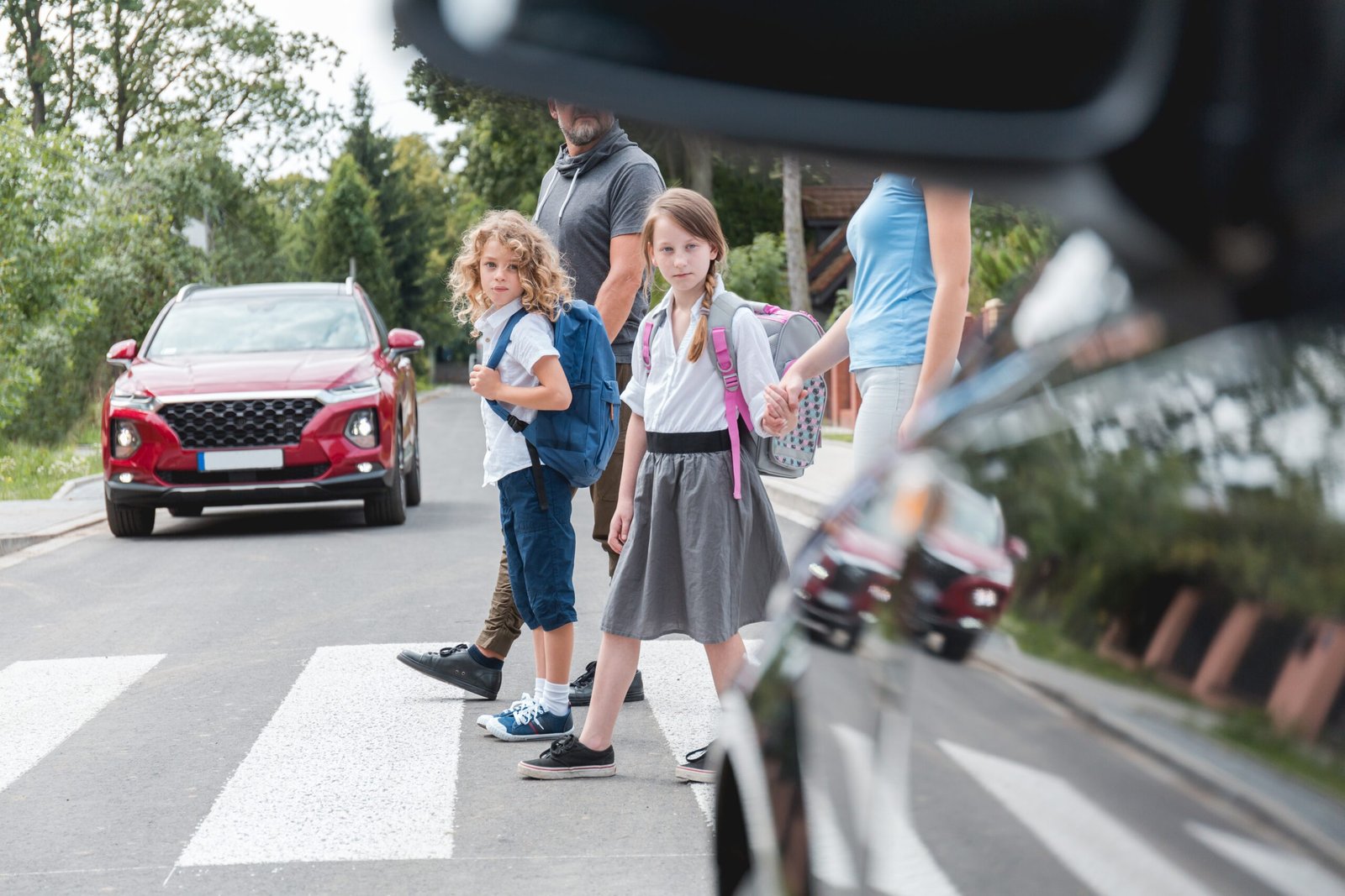 Group of school children goes through the pedestrian crossing in the street, right in front of the car